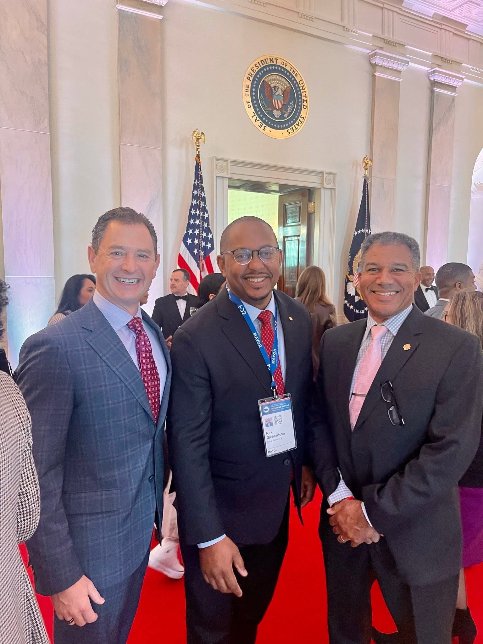 Ray Jackson with two other officials posing indoors in front of a government seal and American flag.